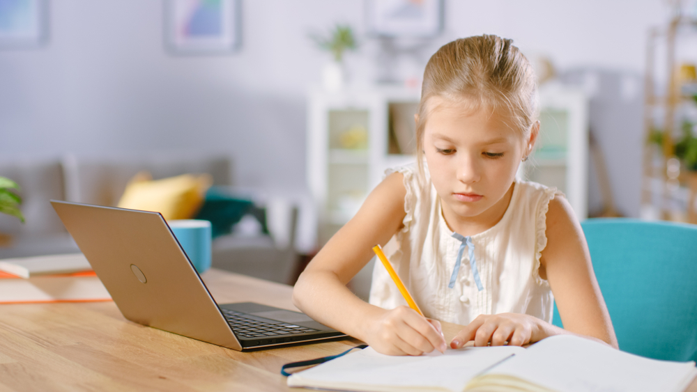 a kid is writing in front of laptop