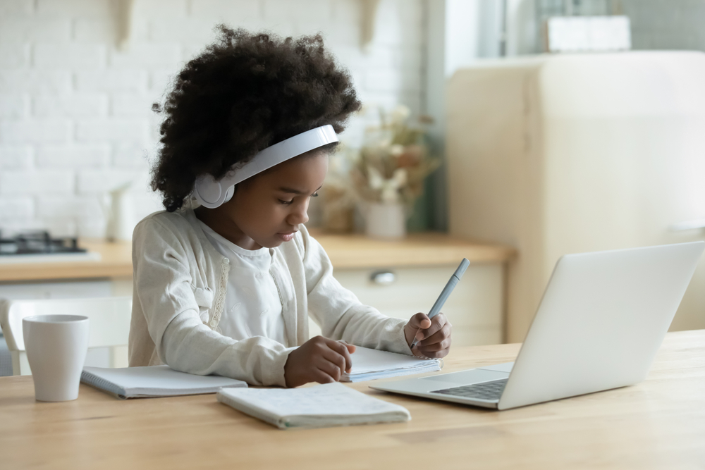 a girl writing in front of a laptop